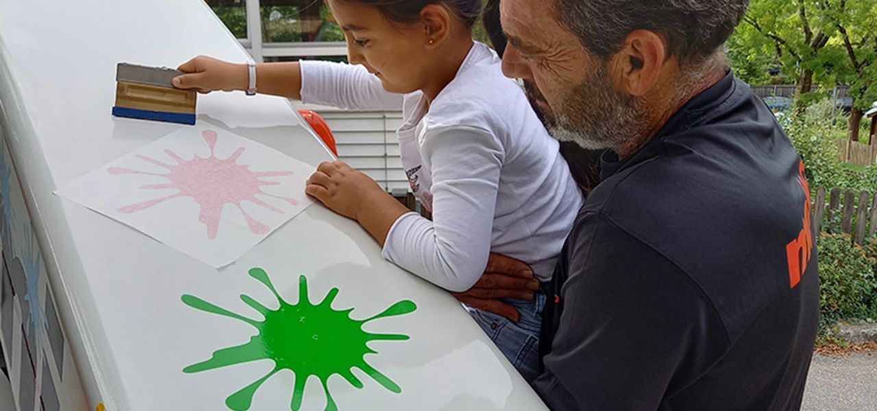 Ein Kind und ein Mitarbeiter bekleben gemeinsam eine Arbeitsbühne von mateco als Teil eines sozialen Projekts