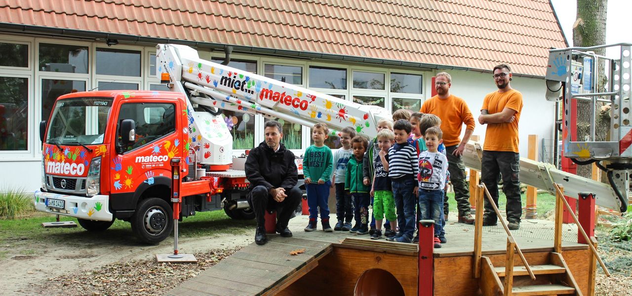 Soziales Engagement von mateco in Mutterstadt: Baumpfleger, mateco-Arbeitsbühne und Kindergartenkinder posieren für ein Gruppenbild im Garten