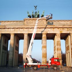 Bauarbeiter in Sicherheitskleidung steht in einer Arbeitsbühne und arbeitet an der Fassade eines Gebäudes unter freiem Himmel.