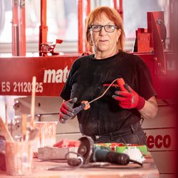 Frau in einer Werkstatt steht vor einer Schere und hält einen Streichpinsel in der Hand, bereit für Arbeiten