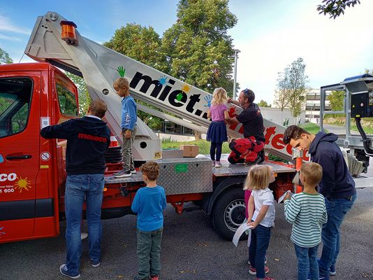 Kindergartenkinder bekleben eine rote Arbeitsbühne im Rahmen eines sozialen Engagement-Projekts von mateco