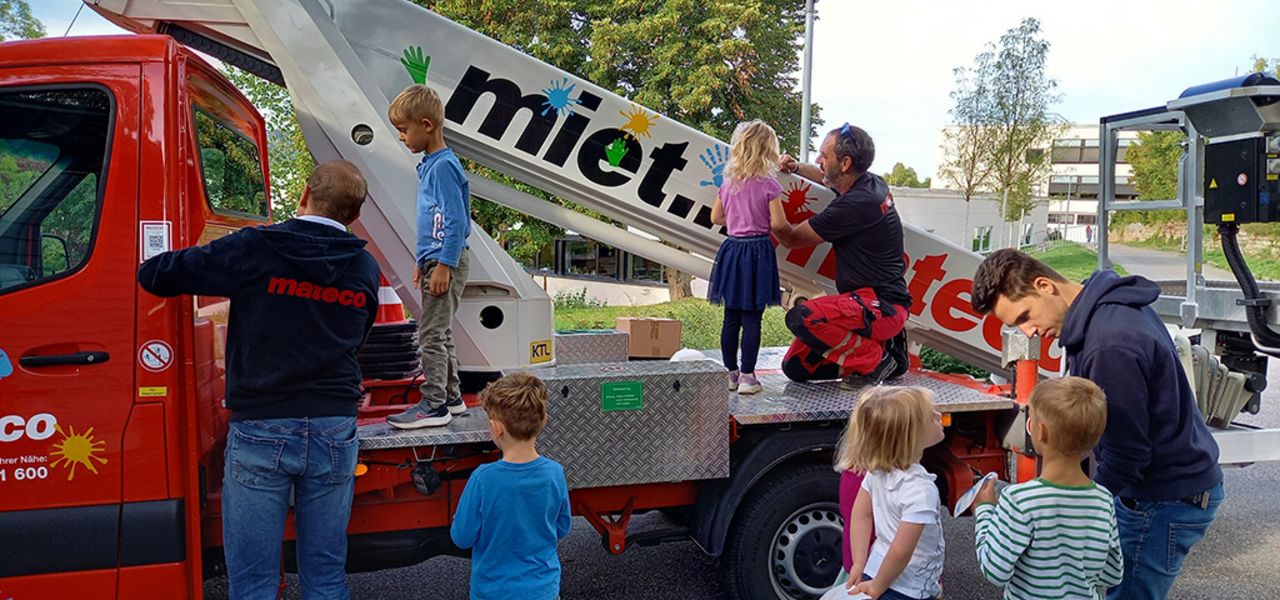 Kindergartenkinder bekleben eine rote Arbeitsbühne im Rahmen eines sozialen Engagement-Projekts von mateco