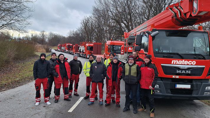 11 Mitarbeiter bei einer Sicherheitsschulung vor roten LKW-Arbeitsbühnen