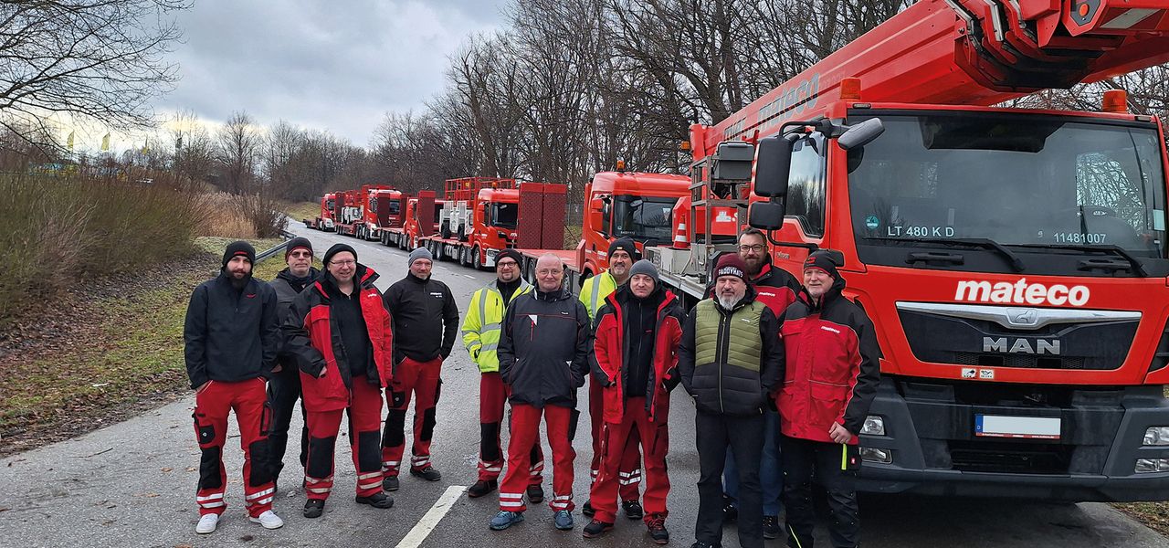 11 Mitarbeiter bei einer Sicherheitsschulung vor roten LKW-Arbeitsbühnen